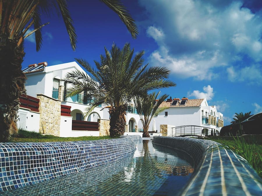 A modern building with a pool, palm trees, and a clear blue sky.