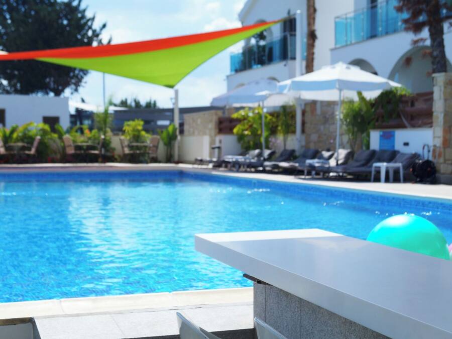 Una piscina con sillones de playa y sombrillas, rodeada por un edificio de fachada de piedra.