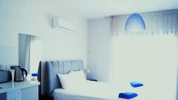 Una habitación de hotel con una cama, un escritorio con un hervidor, una lámpara y una ventana con cortinas.