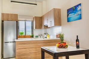Una cocina moderna con armarios de madera, un refrigerador de acero inoxidable, una mesa de comedor con un frutero y copas de vino, y un cuadro de un velero en la pared.