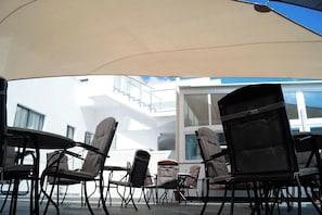 Outdoor seating with chairs and tables under a canopy, overlooking a building with large windows and a balcony. - Latchi Escape Hotel and Suites (Neo Chorio)