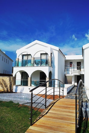 A modern two-story building with a balcony, a wooden deck, and a clear blue sky. - Latchi Escape Hotel and Suites (Neo Chorio)