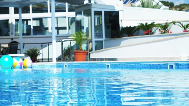 A swimming pool with clear blue water, surrounded by a modern building with large windows and a white exterior. - Latchi Escape Hotel and Suites (Neo Chorio)