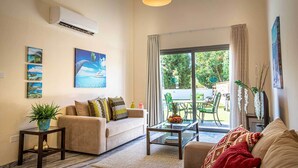 A living room with a sofa, a coffee table, a TV, and a view of the outdoors. - Latchi Escape Hotel and Suites (Neo Chorio)