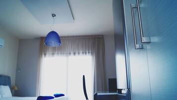 A hotel room with a bed, a desk, a chair, a blue hanging lamp, and a window with curtains.