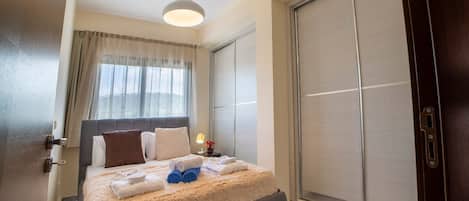 A hotel room with a bed, a nightstand, a lamp, a window with curtains, and a sliding door.