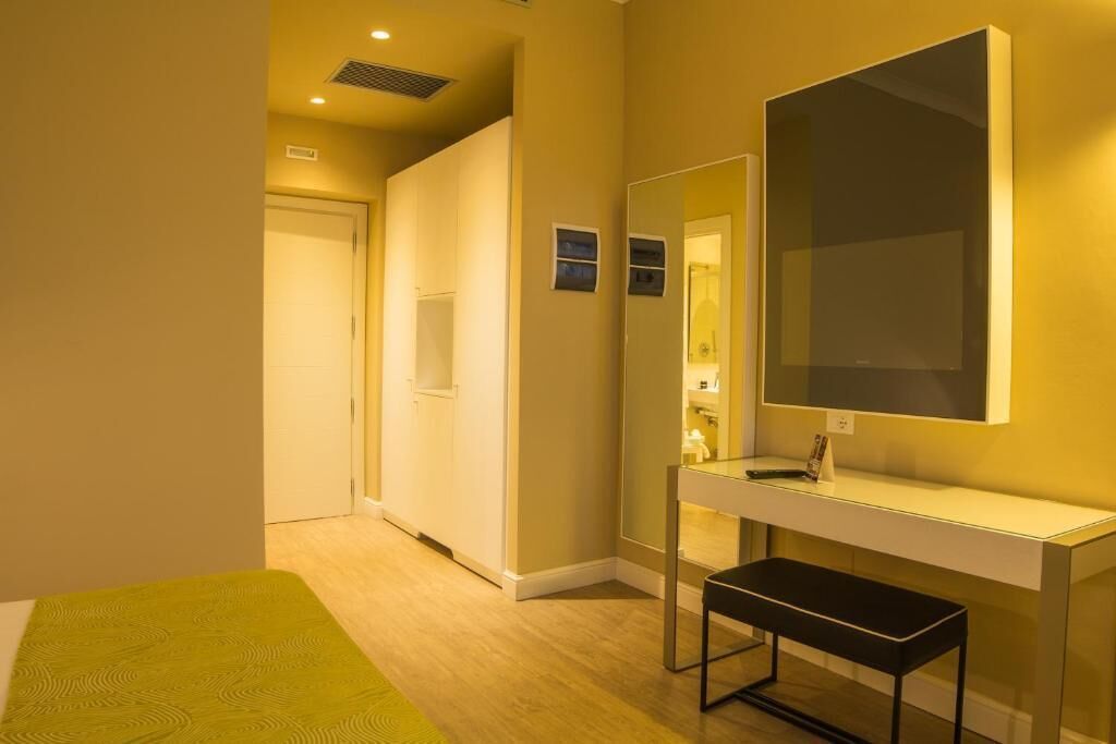 Quarto de hotel com cama, mesa de cabeceira, espelho e banheiro visível por uma porta aberta.