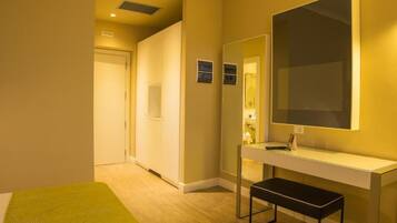 Quarto de hotel com cama, mesa de cabeceira, espelho e banheiro visível por uma porta aberta.