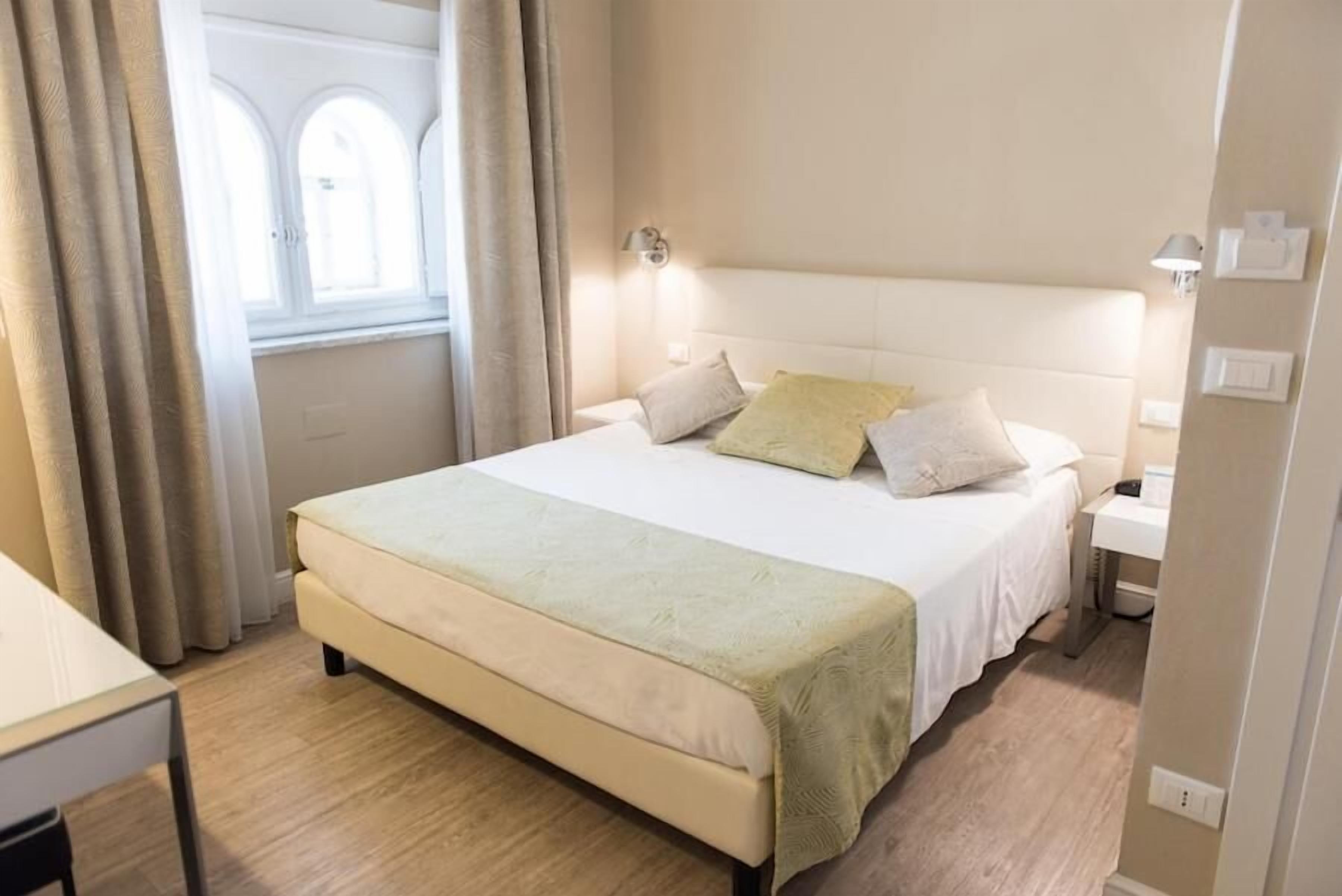Habitación de hotel con una cama grande, una mesita de noche, una lámpara y una ventana con cortinas.