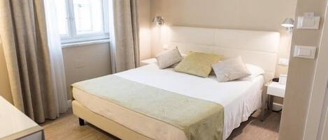 Une chambre d’hôtel avec un grand lit, une table de chevet, une lampe et une fenêtre avec des rideaux.