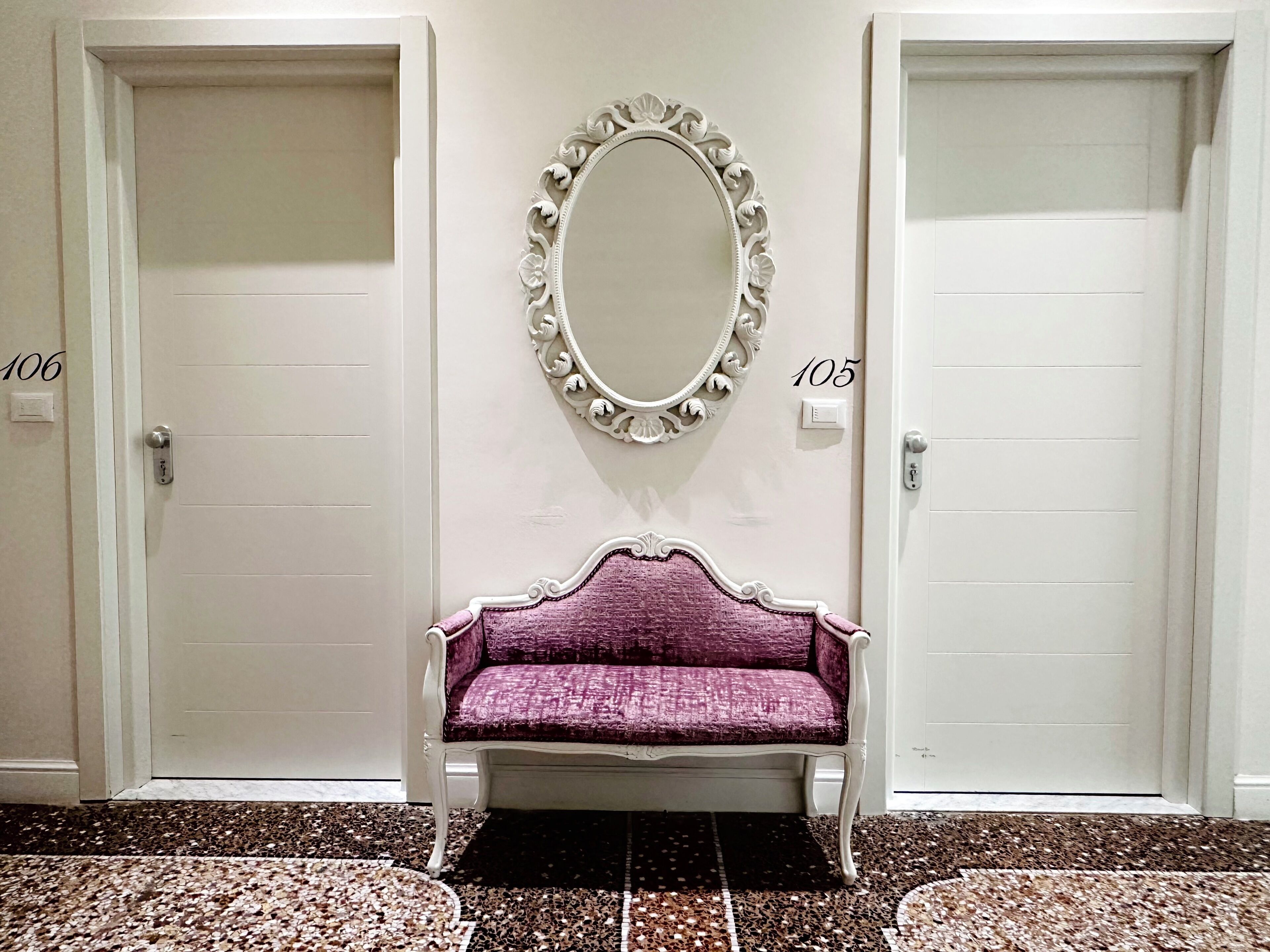 A hallway with two doors labeled 106 and 105, a bench, and a decorative mirror.