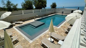 A rectangular swimming pool with a stone deck, surrounded by lounge chairs and umbrellas, overlooking a body of water. - Hotel Universal (Livorno)