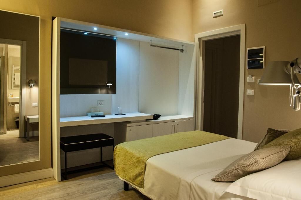 Una habitación de hotel con una cama, un escritorio con espejo y un banco.