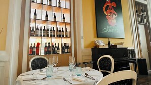 A dining area with a wine rack, a table set for two, and a piano. - Hotel Universal (Livorno)