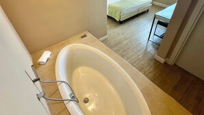A modern bathroom with a large bathtub, a visible bed in the adjacent room, and a view of the sea through a window. - Hotel Universal (Livorno)