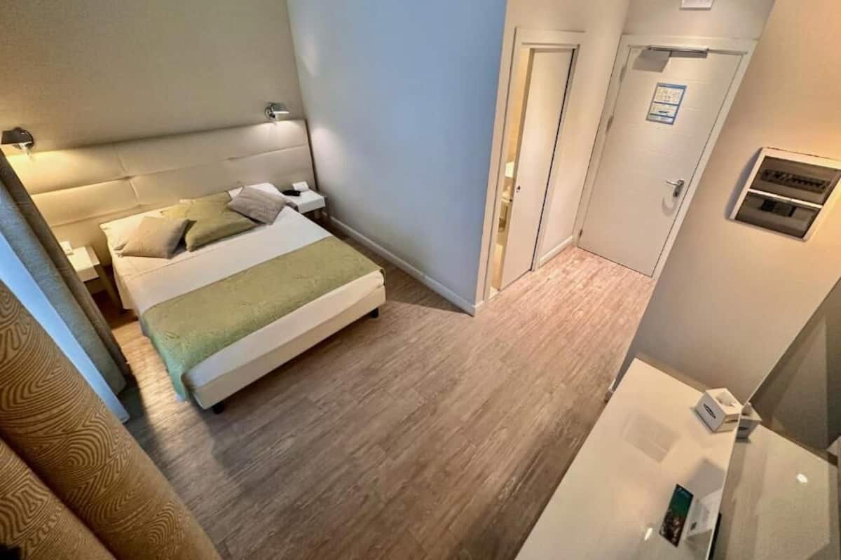 Una habitación de hotel con cama, mesitas de noche, un espejo y una puerta.
