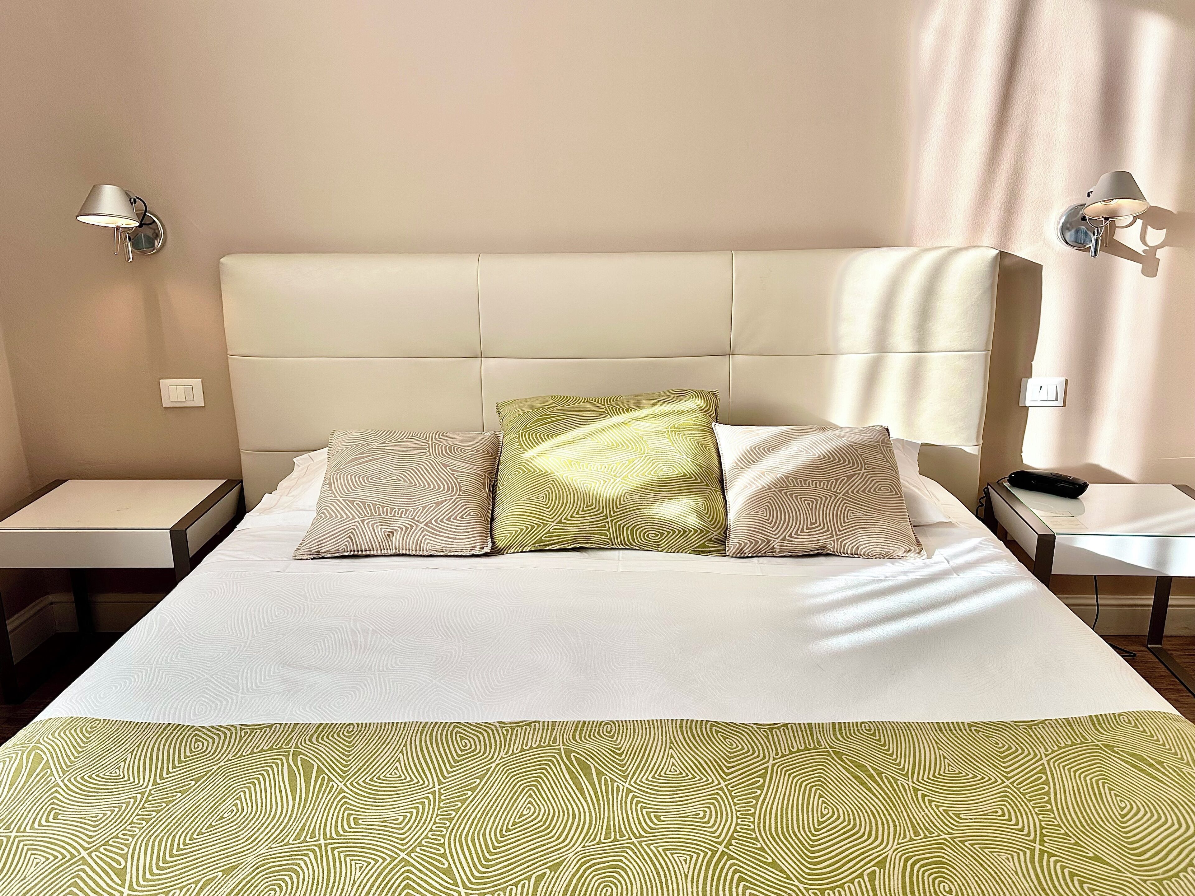 A neatly made bed with patterned pillows, a bedside table, and a wall-mounted lamp.