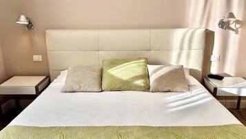 Una cama bien hecha con almohadas estampadas, una mesita de noche y una lámpara de pared.