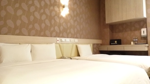 A hotel room with two beds, a bedside table with a radio, and a wall-mounted light fixture. - YPJ Hotel (Kaohsiung)