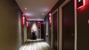 A hotel hallway with striped carpet, dark walls, and red neon signs on the doors. - YPJ Hotel (Kaohsiung)