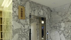 A marble-floored hallway with a mirrored elevator door and a wooden sign. - YPJ Hotel (Kaohsiung)