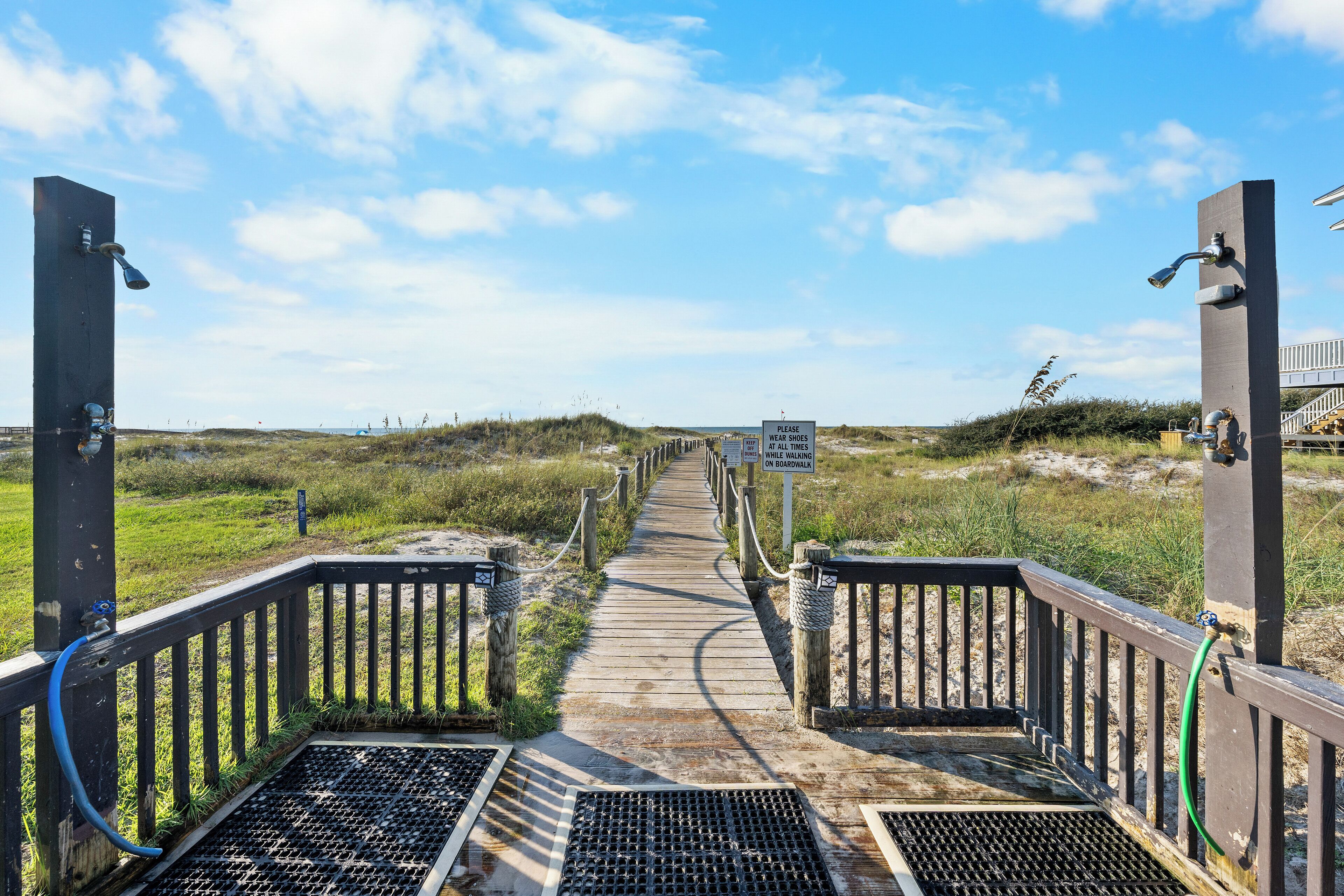 A wooden boardwalk leading to a beach with a sign instructing to wear shoes.