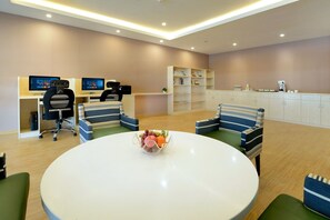 A modern office space with two desks, two chairs, a round table with a fruit bowl, and a bookshelf. - Xiamen Air Maple Hotel (Xiamen)