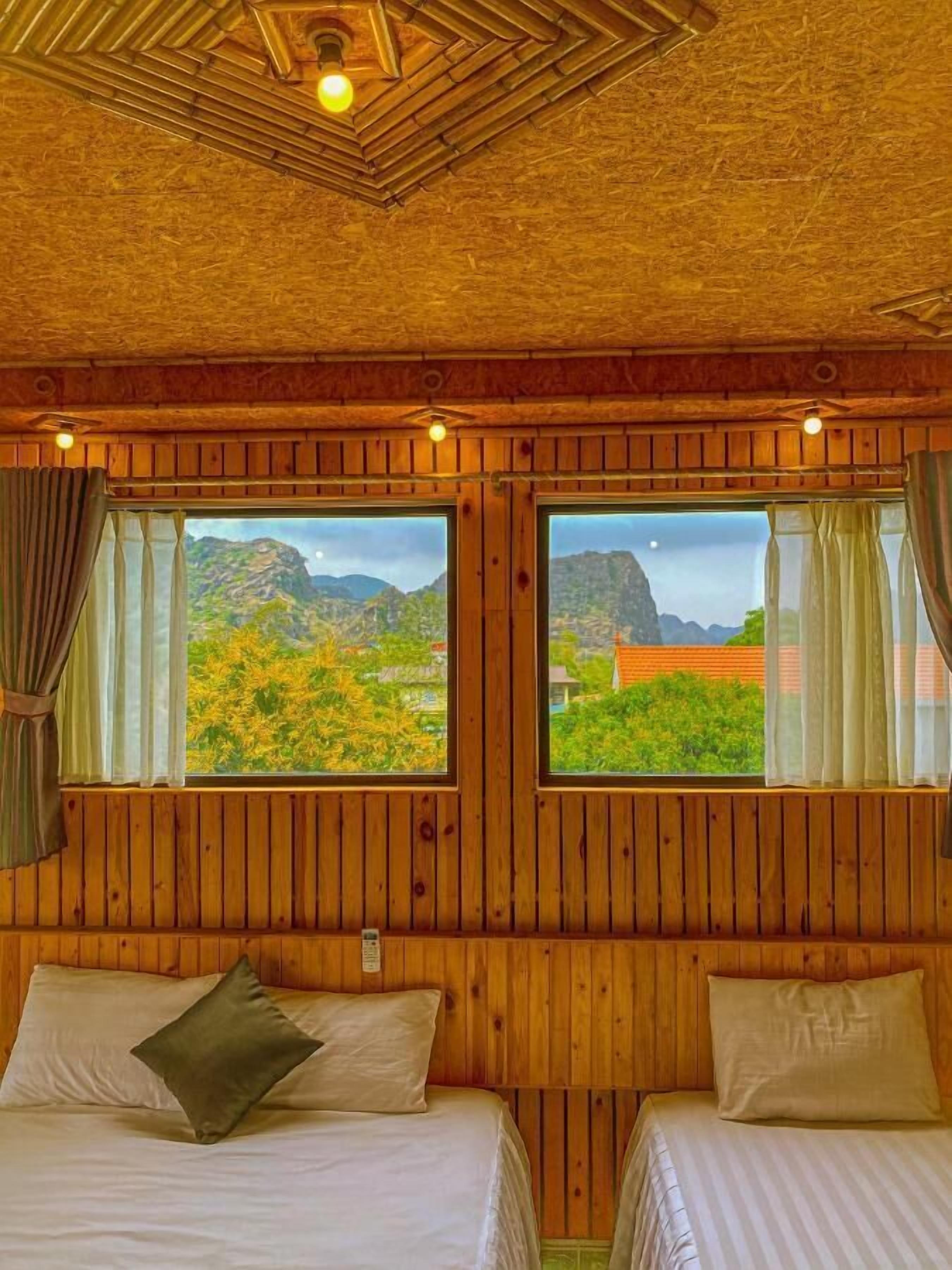 A room with wooden paneling, two beds, a view of mountains, and a ceiling light fixture.