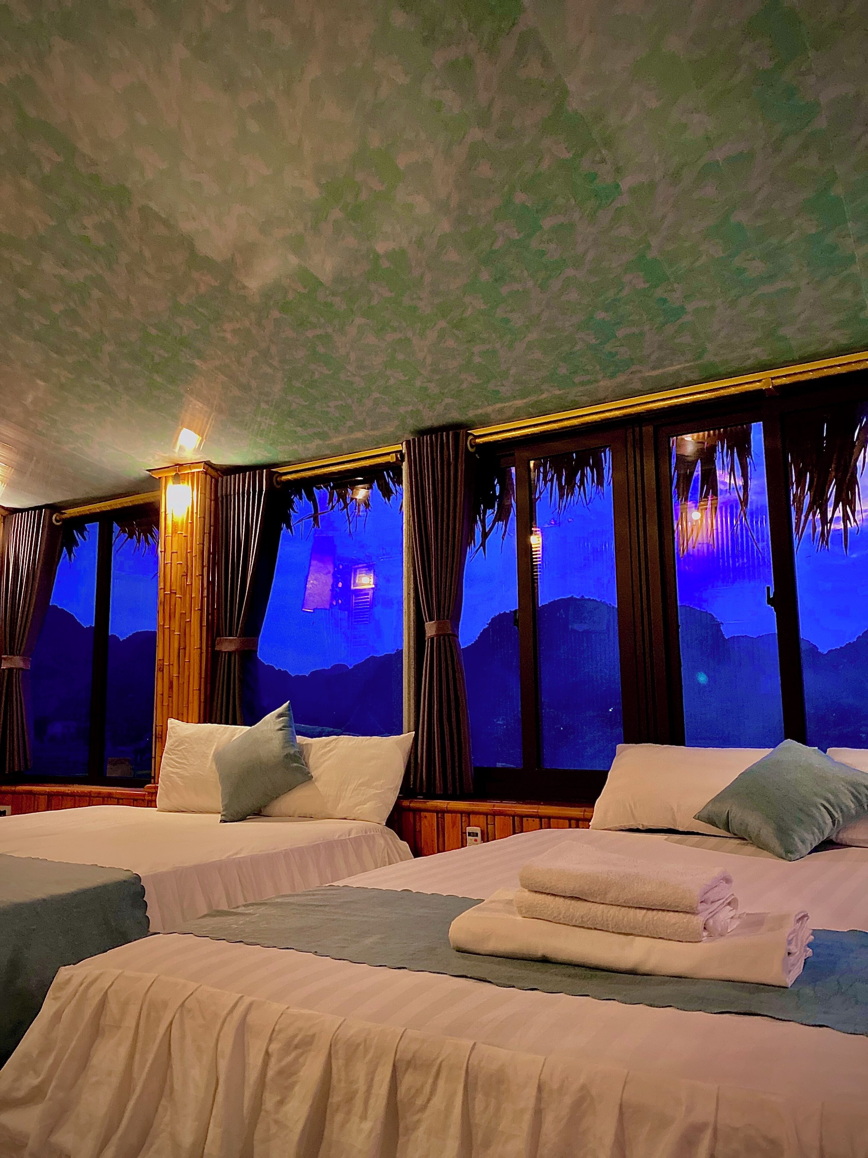 A hotel room with two beds, a large window with a view of the mountains, and a ceiling with a textured pattern.