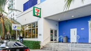 A 7-Eleven convenience store with a blue exterior, a parking sign, and a palm tree in the foreground. - Brickell Bay 3505 (Miami)