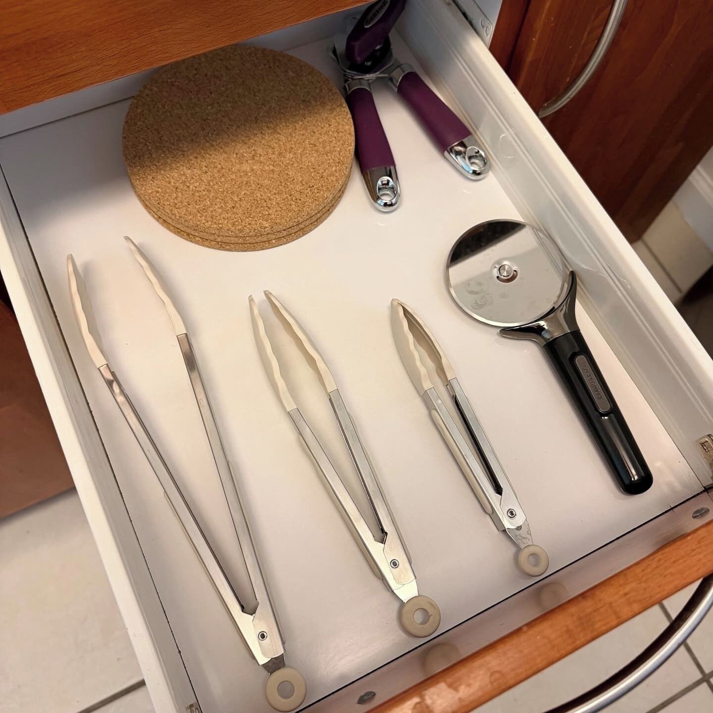A drawer containing various kitchen utensils including a cork, tongs, and a pizza cutter.