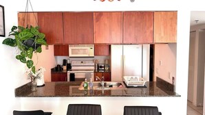 A modern kitchen with wooden cabinets, a granite countertop, a microwave, a refrigerator, and a hanging plant. - Brickell Bay 3505 (Miami)