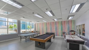 A spacious indoor area with a foosball table, ping pong table, and a pool table. Large windows provide natural light and a view of the city. - Brickell Bay 3505 (Miami)