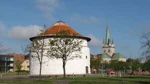 A historic building with a round tower and a church with a green spire in the background. - Fredrikshavn Hotel First Partner (Frederikshavn)