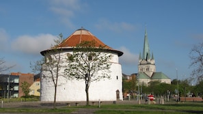 A historic building with a round tower and a church with a green spire in the background. - Fredrikshavn Hotel First Partner (Frederikshavn)