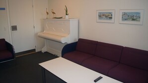 A room with a white piano, a red couch, a white table, and two framed pictures on the wall. - Fredrikshavn Hotel First Partner (Frederikshavn)