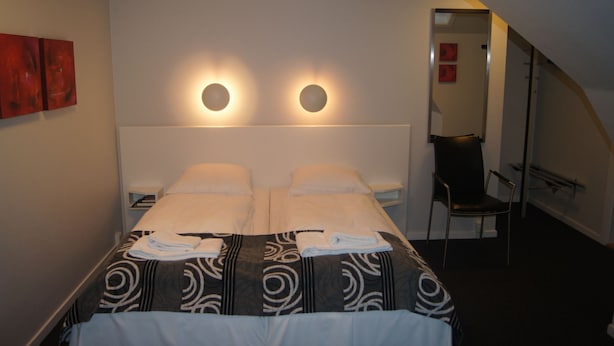 Una camera d'albergo con un letto, due comodini, una sedia e uno specchio.