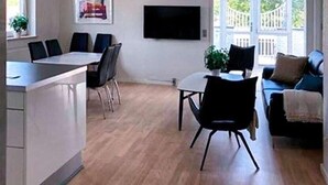 Una cucina moderna con zona pranzo, una TV a muro e un'ampia finestra con vista sul verde.