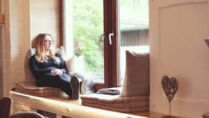 Une personne assise sur un banc près d’une fenêtre, avec vue sur la verdure à l’extérieur.