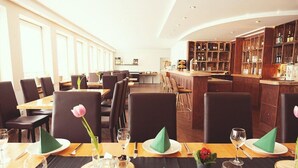 Een restaurant met meerdere tafels, donkere stoelen en een bar voorzien van houten planken.
