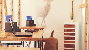 Un bureau en bois avec un ordinateur portable, un téléphone intelligent et un porte-stylos. Il y a une étagère fixée au mur avec une plante et une armoire en bois avec des tiroirs.