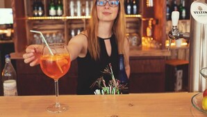 Un barman tenant un verre à cocktail dans un bar, avec une tireuse à bière Veltin et une bouteille de bière en arrière-plan.