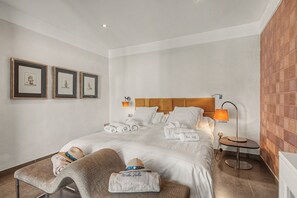 Una habitación de hotel con una cama, dos cuadros en la pared, una lámpara de noche y una mesita con una lámpara.