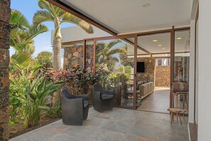 Un patio al aire libre con muros de piedra, plantas tropicales y mobiliario moderno.