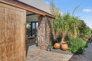 Un edificio moderno con puerta de madera, pared de piedra y jardín con plantas y macetas.