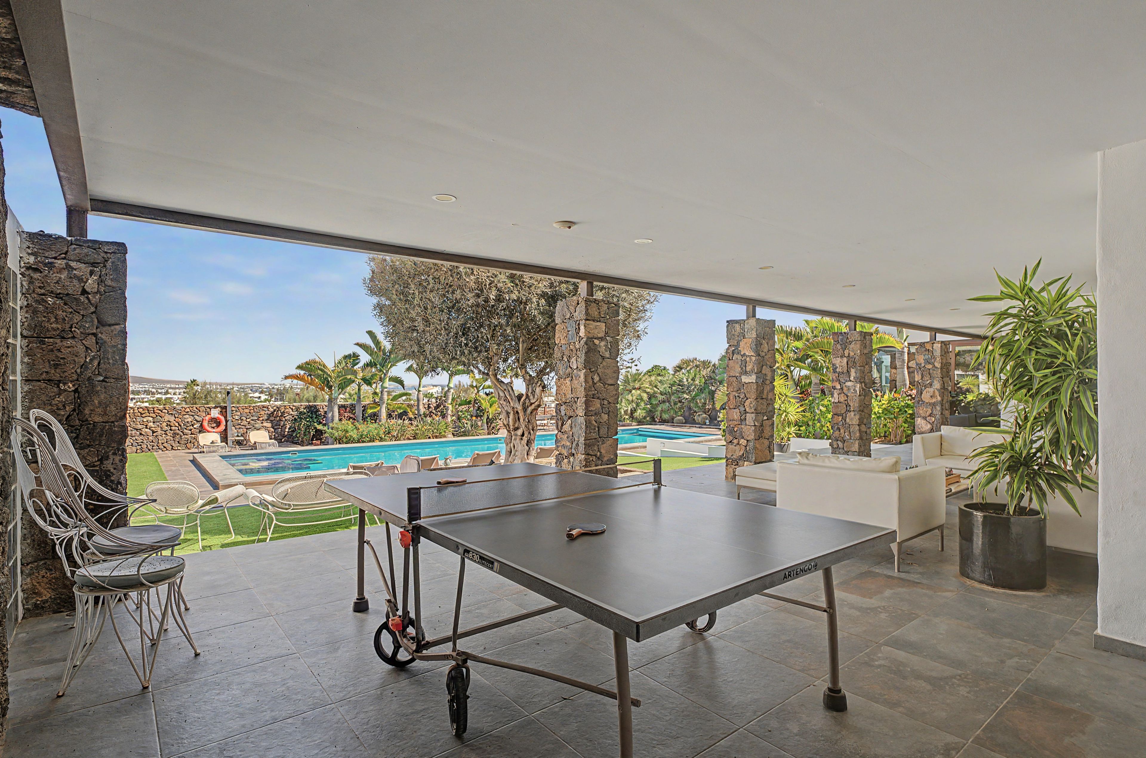 Una mesa de tenis de exterior con vista a una piscina y palmeras.