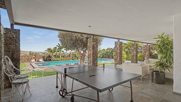 Una mesa de tenis de exterior con vista a una piscina y palmeras.