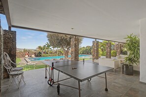 Una mesa de tenis de exterior con vista a una piscina y palmeras.