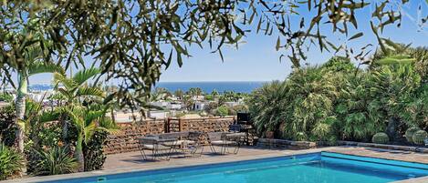 Área de piscina com vista para o mar, cercada por vegetação e espaço para churrasco.