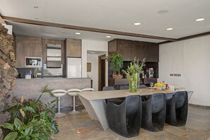 Cocina moderna con comedor, destacando una pared de piedra, horno empotrado e isla central con asientos.